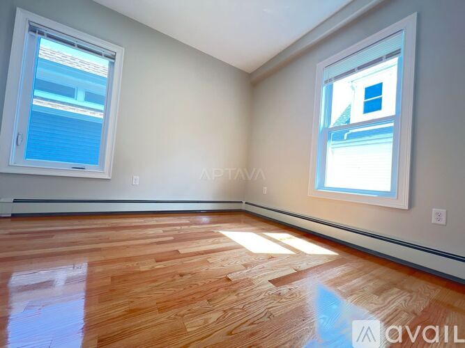 A room with wooden flooring and two windows.