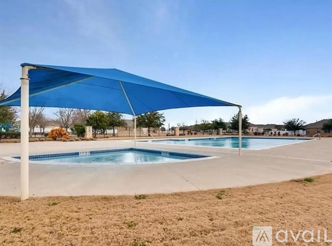 A pool with a blue canopy is surrounded by dry grass.
