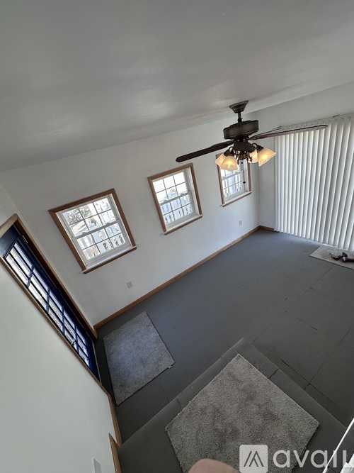A living room with a ceiling fan and three windows.