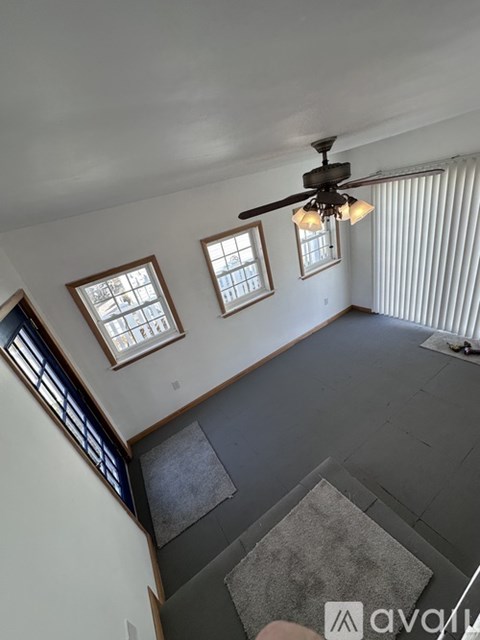A living room with a ceiling fan and three windows.