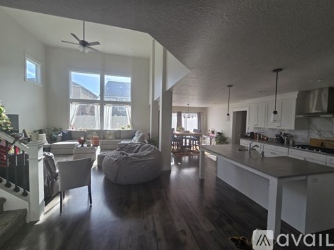 A living room with a grey bean bag chair and a kitchen area with white cabinets.