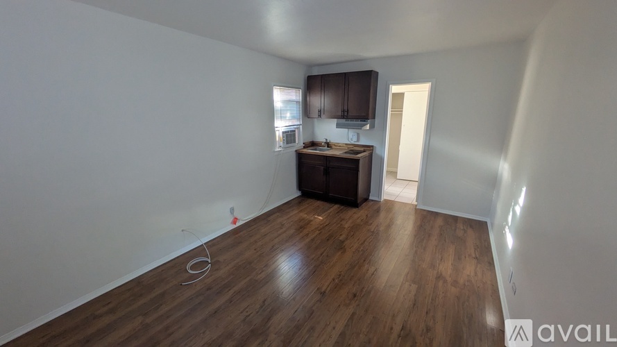A room with wooden flooring and a kitchenette in the corner.