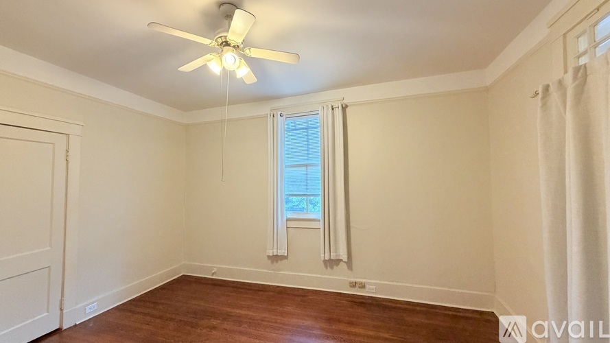 A room with a ceiling fan and a window with white curtains.