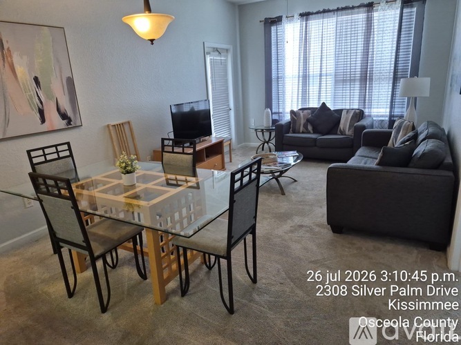 A living room with a glass table and chairs, a couch, and a television.