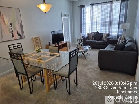 A living room with a glass table and chairs, a couch, and a television.