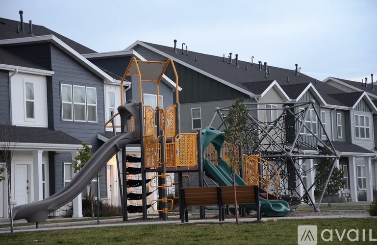 A playground with a green slide and a wooden structure is in front of a row of houses.