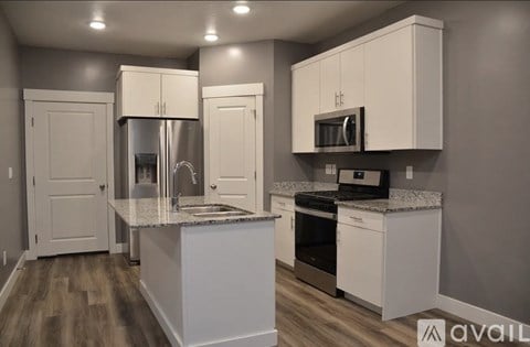 A kitchen with white cabinets and appliances, a sink, and a refrigerator.