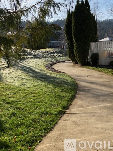 A sidewalk curves through a grassy area with trees and a house in the background.