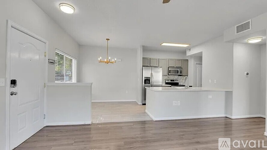 A well-lit, spacious kitchen and living room with a chandelier and hardwood floors.