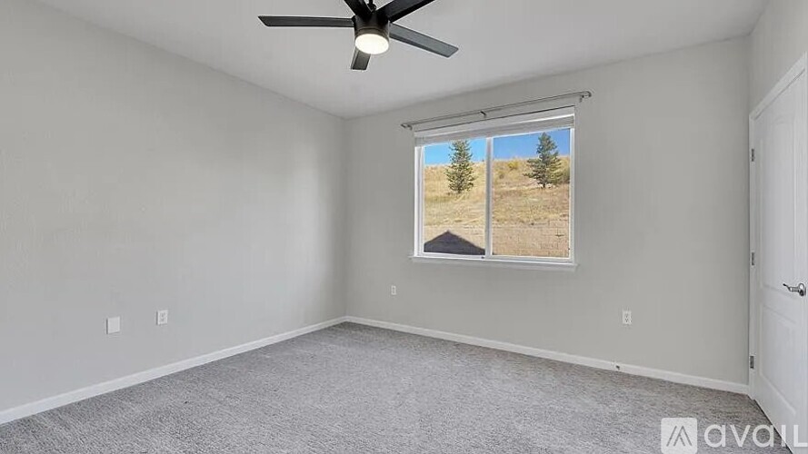 A room with a ceiling fan and a window showing a view of a house and trees.