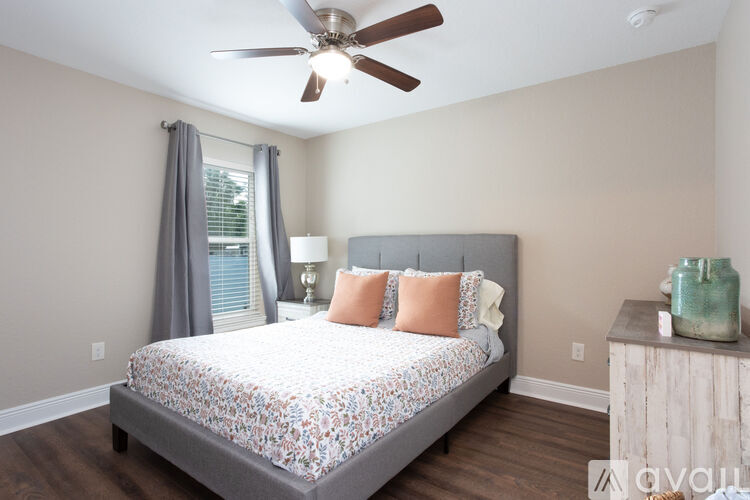 A bedroom with a bed, a ceiling fan, and a nightstand with a green vase on it.