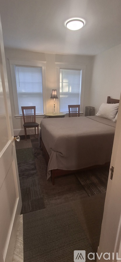 A bedroom with a bed, two chairs, and a lamp.