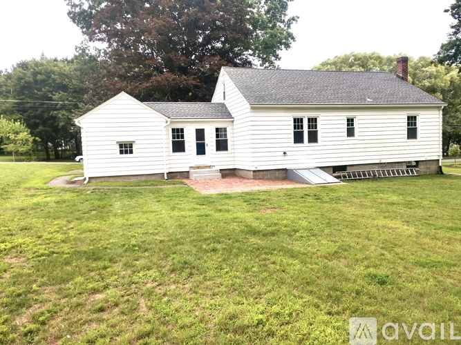 A white house with a black roof and a chimney is surrounded by a grassy lawn.