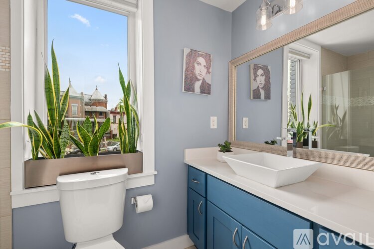 A bathroom with a white toilet, blue cabinetry, and a large mirror.