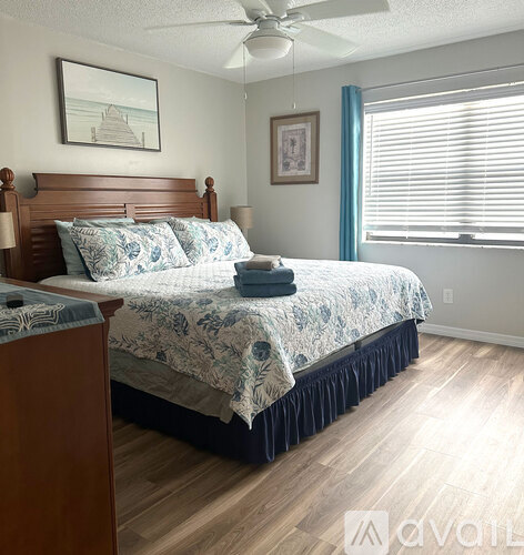 A bedroom with a bed, a ceiling fan, and two pictures on the wall.