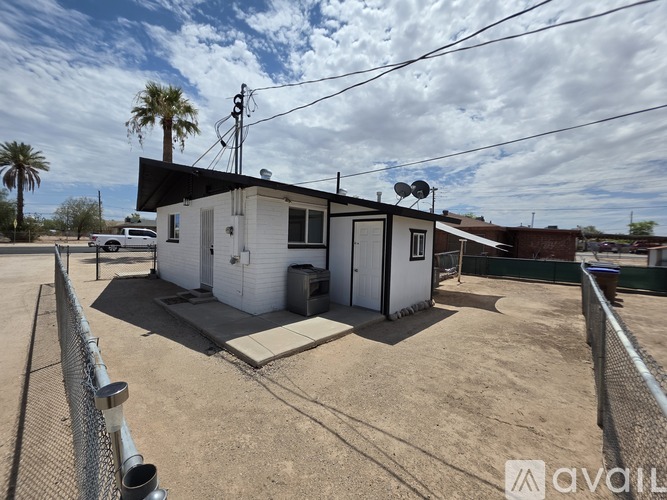 A small white building with a black roof is surrounded by a chain link fence.