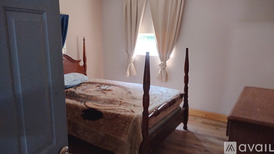 A bedroom with a bed, wooden bed frame, and a window with curtains.