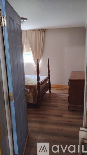 A bedroom with a bed, wooden floor, and a window with curtains.