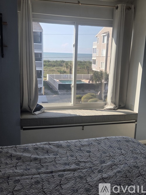 A bedroom with a view of the beach and a building across the way.