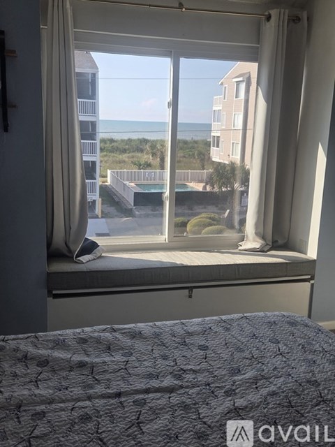 A bedroom with a view of the beach and a building across the way.