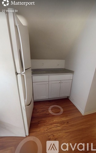 A white refrigerator in a kitchen with wooden floors.