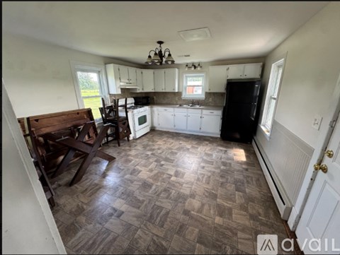 A kitchen with a black fridge, white cabinets, and a wooden table.