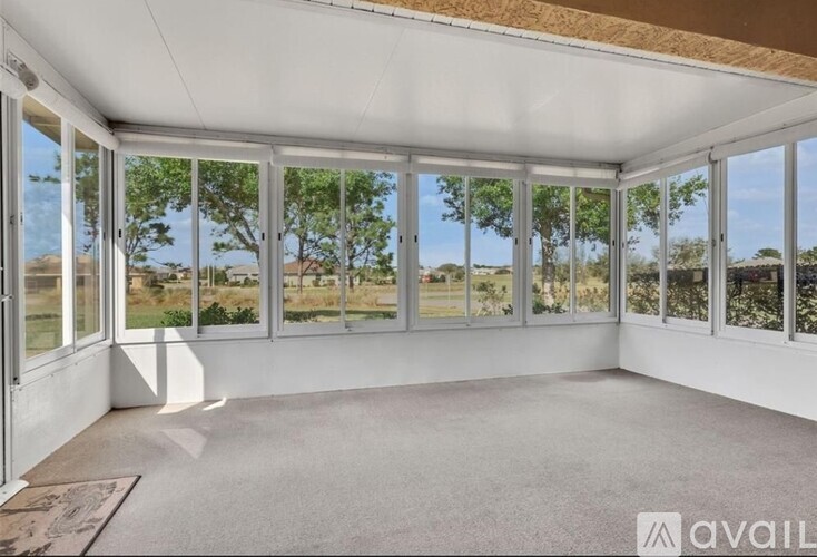 A sunroom with a carpeted floor and large windows overlooking a grassy area.