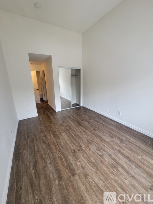 A room with wooden flooring and white walls, with a doorway leading to another room.