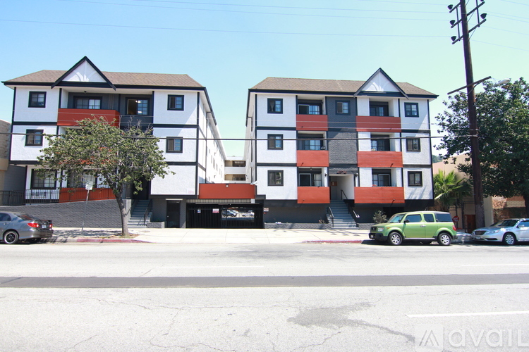 Two apartment buildings with cars parked in front.