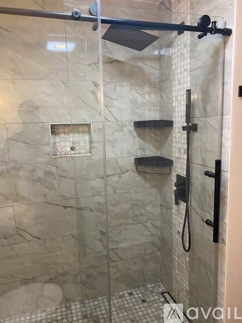 A shower with a glass door and a black handle.