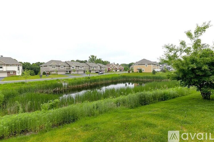 A grassy area with a pond and houses in the background.