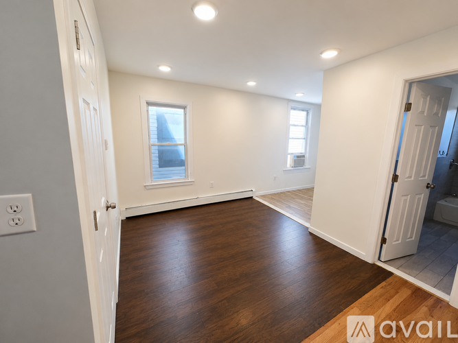 A room with wooden floors and white walls, with a window and a door visible.