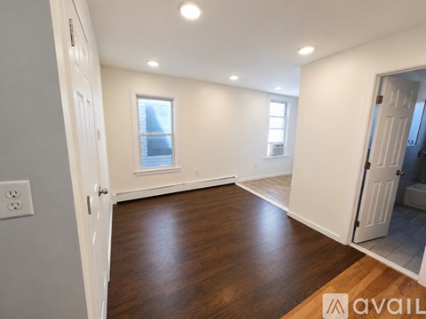 A room with wooden floors and white walls, with a window and a door visible.