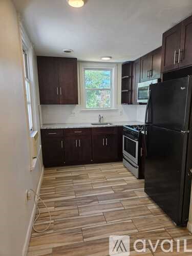 A kitchen with a black fridge and wooden flooring.