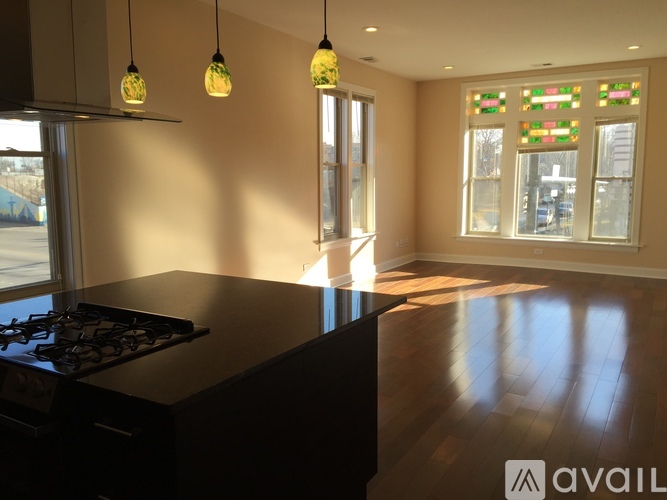 A kitchen with a black countertop and a stove, with three hanging lights and a window with a view of a parking lot.