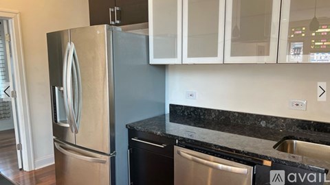 A stainless steel refrigerator in a kitchen with a black granite countertop.