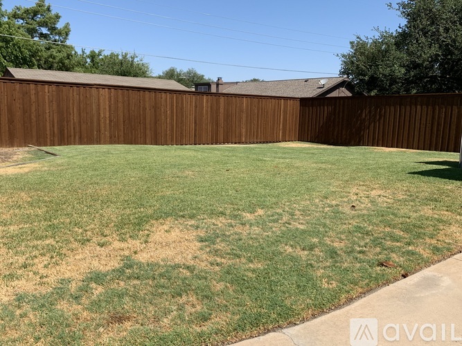 A backyard with a brown fence and patches of brown grass.
