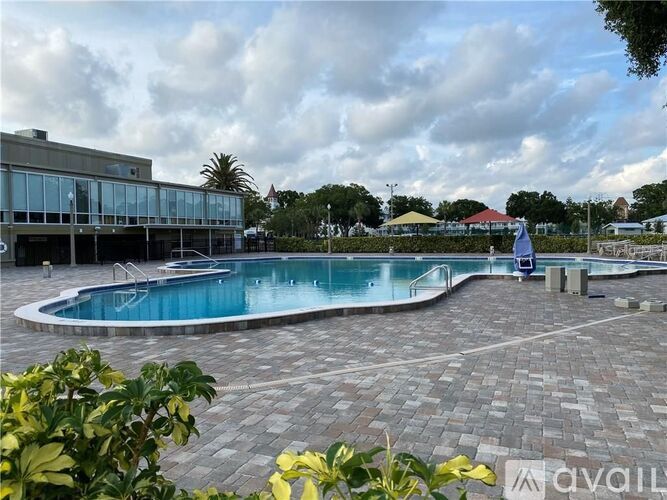 A large outdoor swimming pool surrounded by a brick patio and a building in the background.