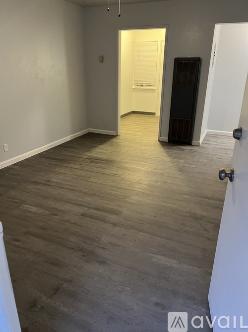A room with wooden flooring and white walls, with a door on the right side.