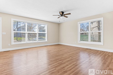 A spacious room with a ceiling fan and two windows.