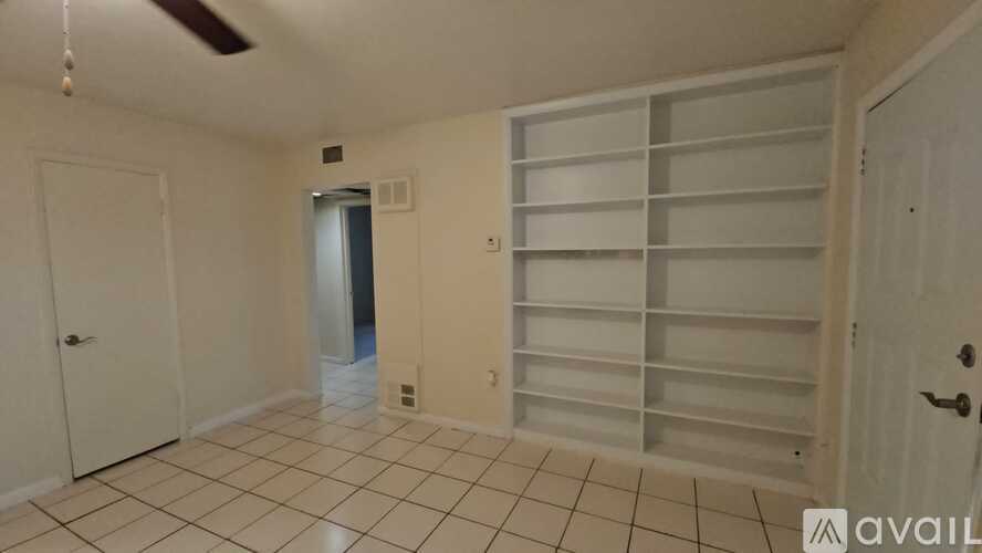 A room with a white door, a white ceiling fan, and a white tiled floor.