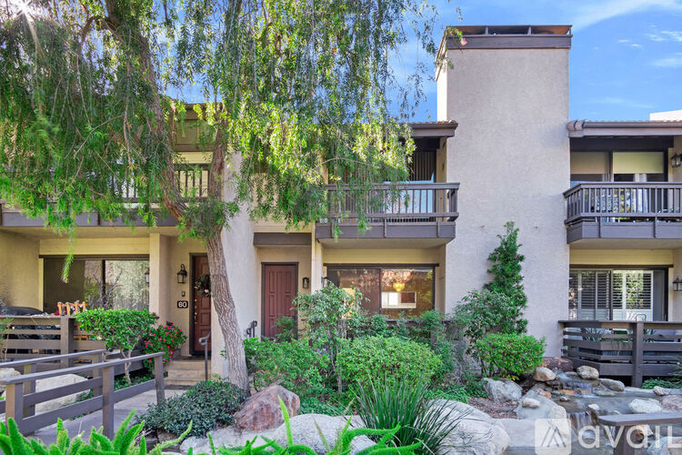 A sunny day at a two-story house with a balcony and a tree in front.