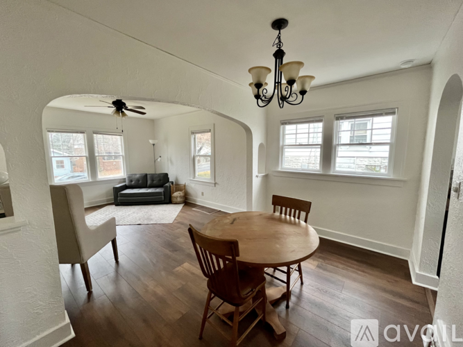 A living room with a wooden table and chairs, a couch, and a chandelier.