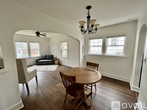 A living room with a wooden table and chairs, a couch, and a chandelier.
