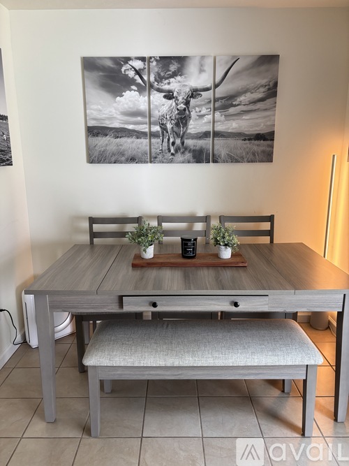A grey table with a bench and a painting of a bull on the wall.