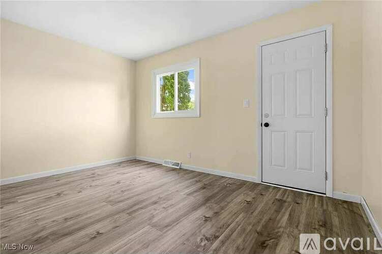 A room with a white door and a window with a view of trees.