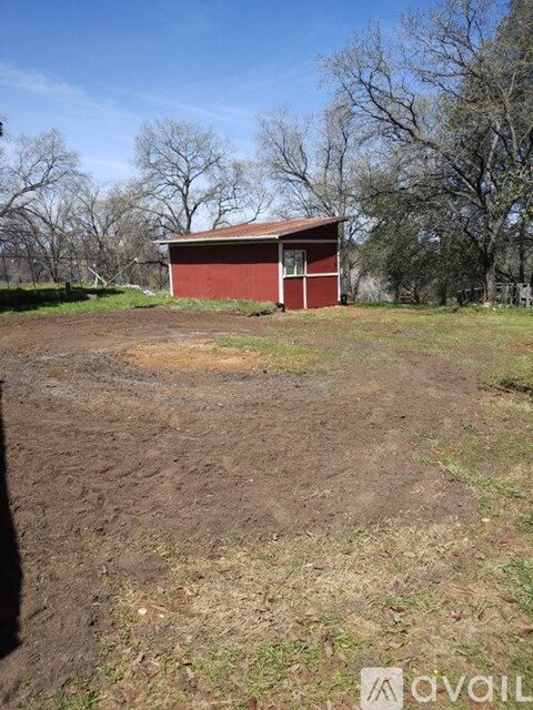 A red barn sits in a field with trees in the background.