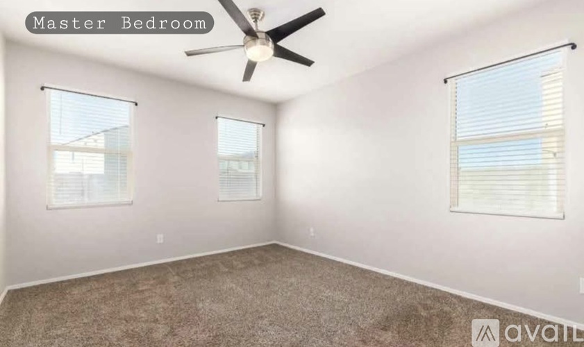 A spacious master bedroom with a ceiling fan and two windows.