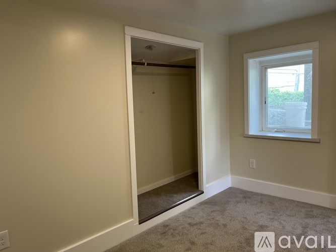 A room with a carpeted floor and a window with a view of a building outside.