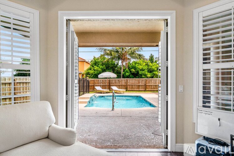 A white couch is in the foreground of a room with a view of a pool and a fence.